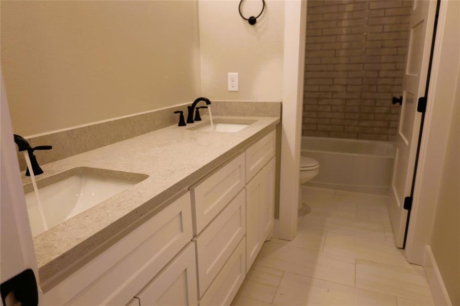 Full bathroom with dual vanity, toilet, tiled shower / bath, and tile patterned flooring