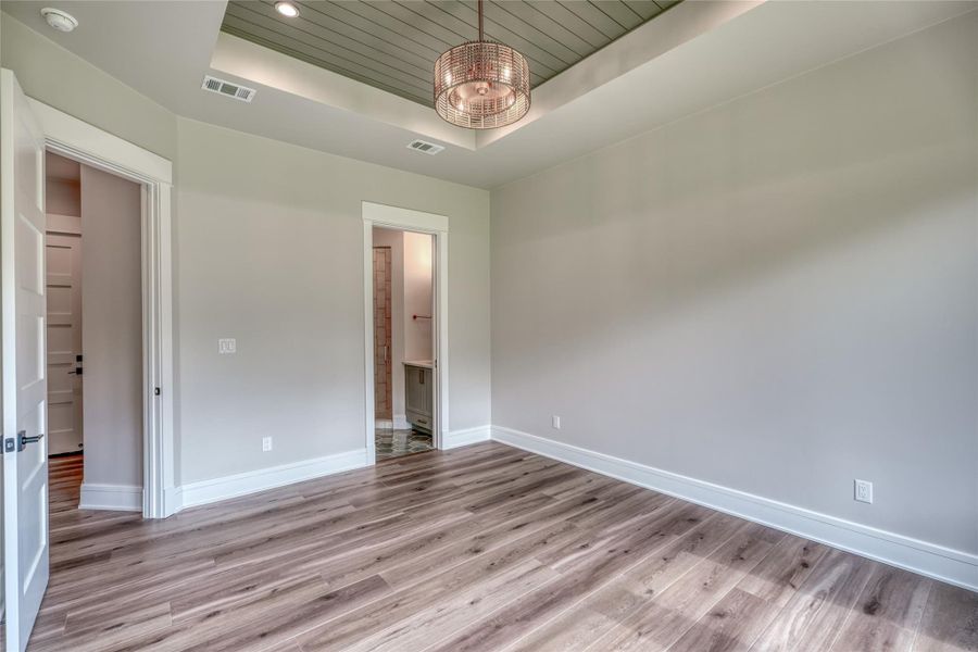 Unfurnished bedroom featuring a tray ceiling, baseboards, a chandelier, wood finished floors, and wooden ceiling