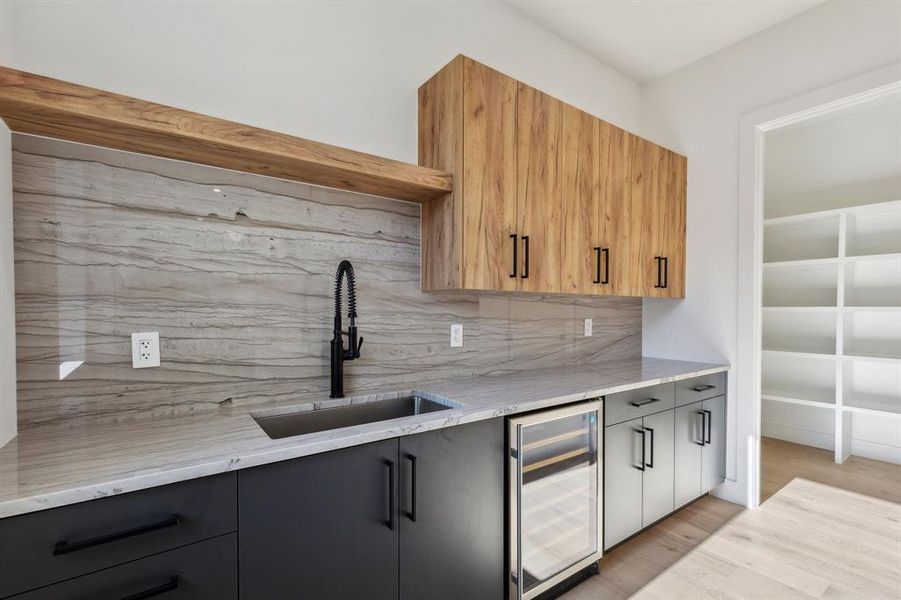 Kitchen with tasteful backsplash, sink, beverage cooler, light stone counters, and light hardwood / wood-style floors