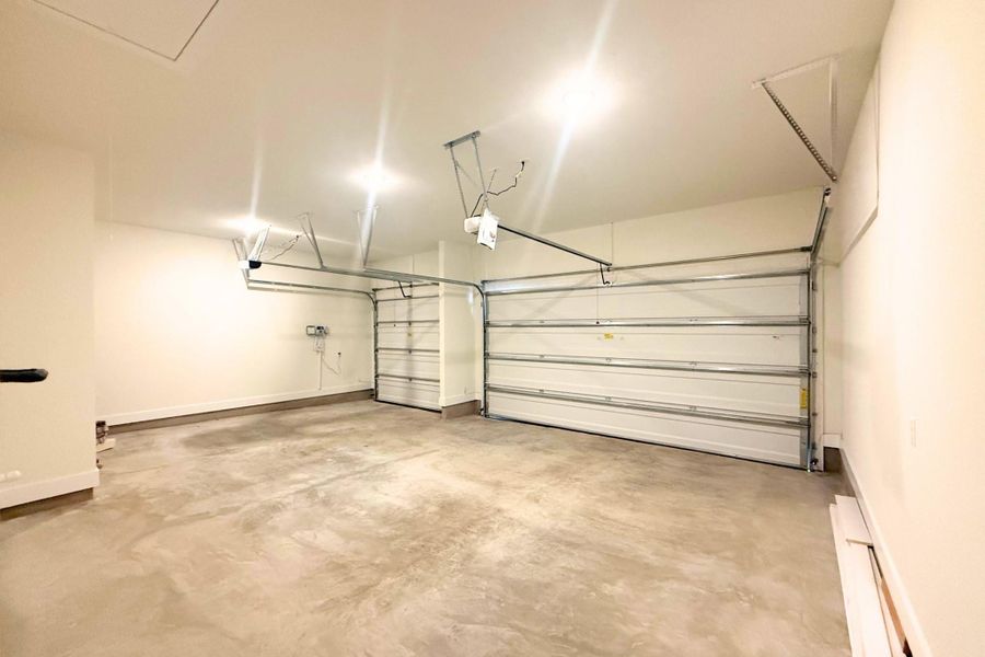 Spacious garage featuring two overhead doors, concrete flooring, ample overhead lighting, clean white walls, and an overhead access panel