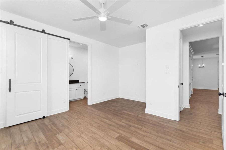 Unfurnished bedroom featuring a barn door, light wood-style floors, baseboards, and a chandelier Unfurnished bedroom featuring a barn door, light wood-style floors, baseboards, and a chandelier