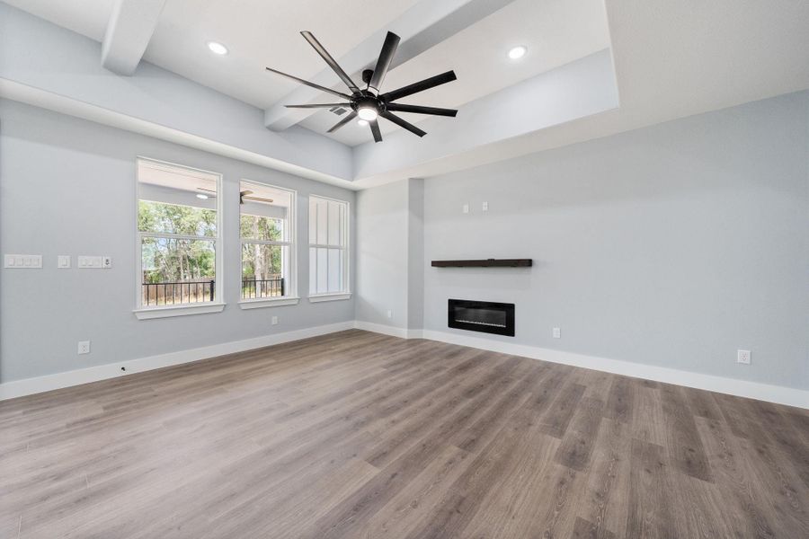Spacious room featuring wood-finish flooring, a contemporary fireplace with a floating wood mantel, and a multi-blade ceiling fan