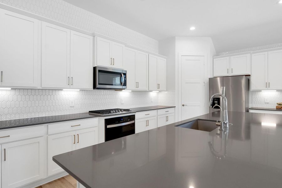 The polished mosaic backsplash extending to the ceiling, combined with under-cabinet lighting, creates a luxurious ambiance.