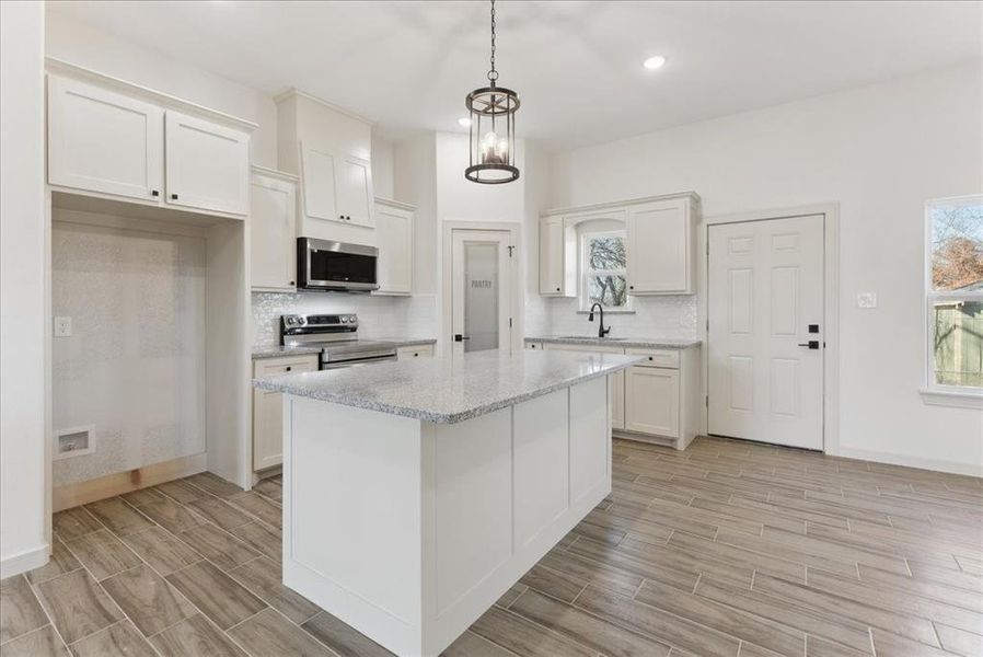 Kitchen featuring a kitchen island, white cabinets, pendant lighting, and appliances with stainless steel finishes