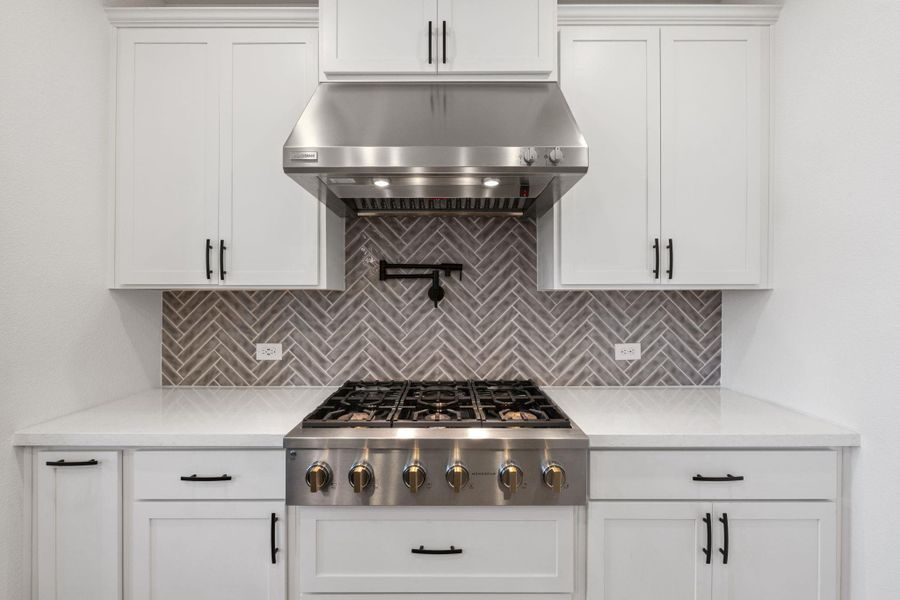 Kitchen with white cabinetry, under cabinet range hood, stainless steel gas stovetop, and quartz countertops