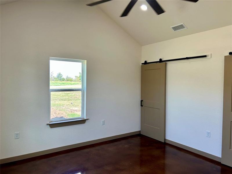 Unfurnished bedroom featuring a barn door, concrete floors, vaulted ceiling, a ceiling fan, and recessed lighting