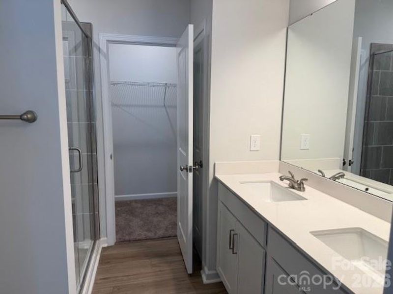 Primary Bath features dual sink vanity and tile shower with semi-frameless shower door and large walk-in-closet