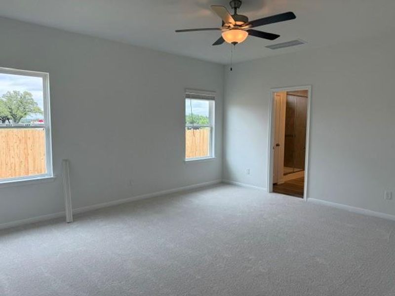 Spacious room featuring light-toned carpeting, two windows with white trim, and a ceiling fan with integrated lighting