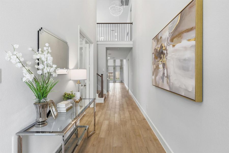 This impressive foyer offers a stunning first impression with soaring ceilings, designer lighting, elegant wood-look tile flooring, and an open sightline that draws your eye toward the spacious living areas beyond.