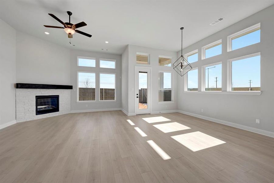 Unfurnished living room featuring ceiling fan, a fireplace, suspended lighting, and light wood-style flooring Unfurnished living room featuring ceiling fan, a fireplace, suspended lighting, and light wood-style flooring