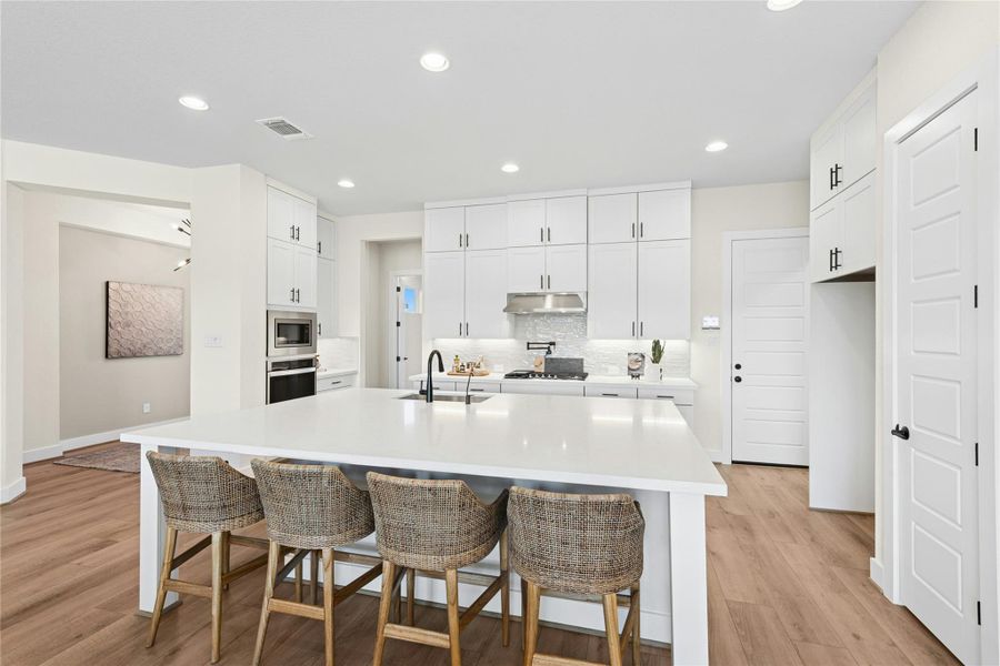 Kitchen with decorative backsplash, white cabinets, recessed lighting, a kitchen bar, and light wood finished floors Kitchen with decorative backsplash, white cabinets, recessed lighting, a kitchen bar, and light wood finished floors