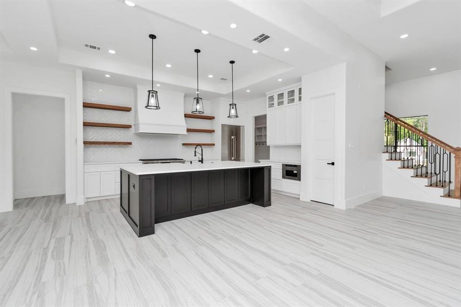 Take a look at the sleek black countertops, and contrasting white cabinetry. It features a center island, open shelving, stainless steel appliances, and pendant lighting.