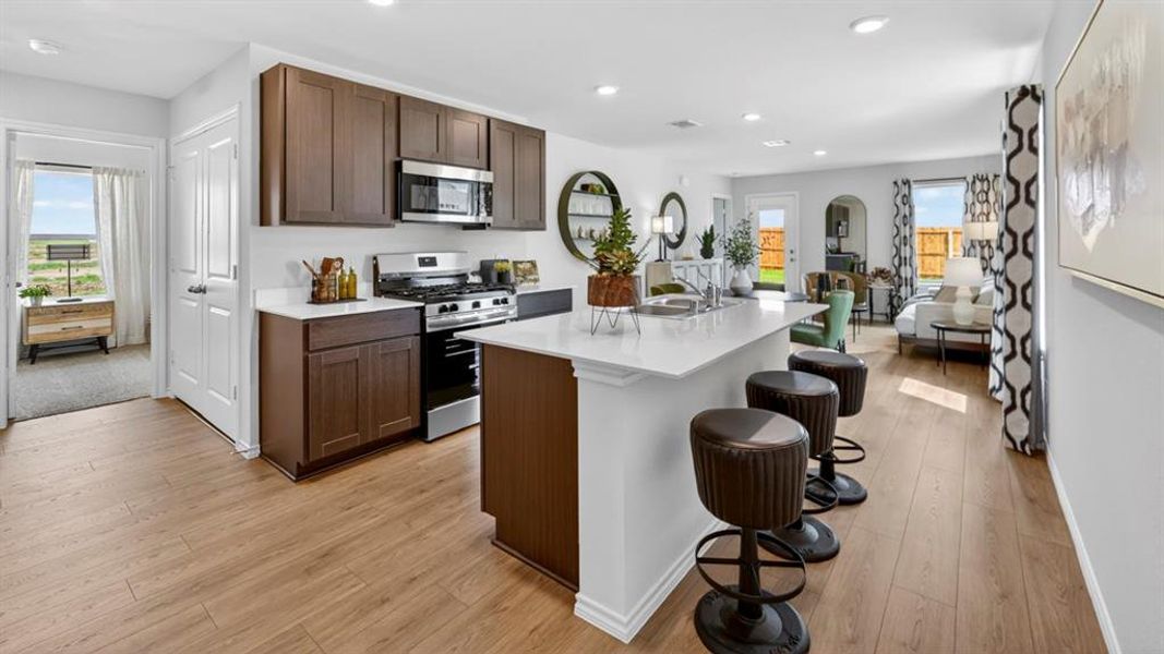 Open-concept kitchen featuring wood-finish flooring, dark wood cabinetry, white countertops, and stainless steel appliances Open-concept kitchen featuring wood-finish flooring, dark wood cabinetry, white countertops, and stainless steel appliances