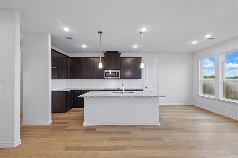 Kitchen featuring stainless steel microwave, a sink, dark brown cabinetry, light wood-style flooring, and recessed lighting Kitchen featuring stainless steel microwave, a sink, dark brown cabinetry, light wood-style flooring, and recessed lighting