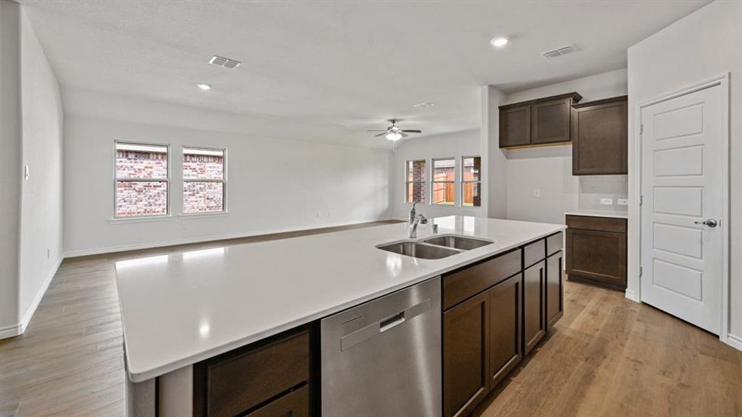 Kitchen with dishwasher, a kitchen island with sink, open floor plan, dark wood finish cabinets, and light wood-style floors