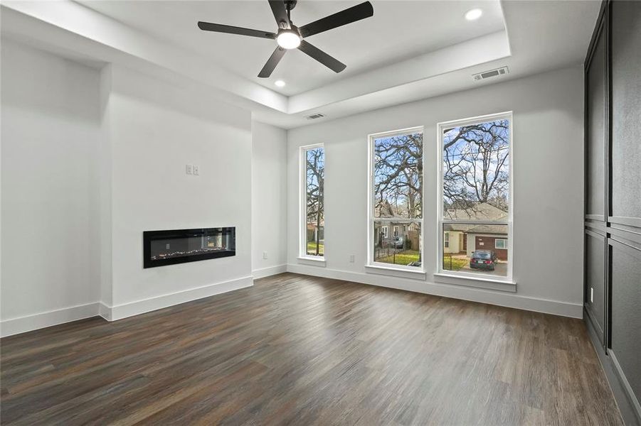 Unfurnished living room with dark wood-type flooring, a glass covered fireplace, a ceiling fan, recessed lighting, and a raised ceiling