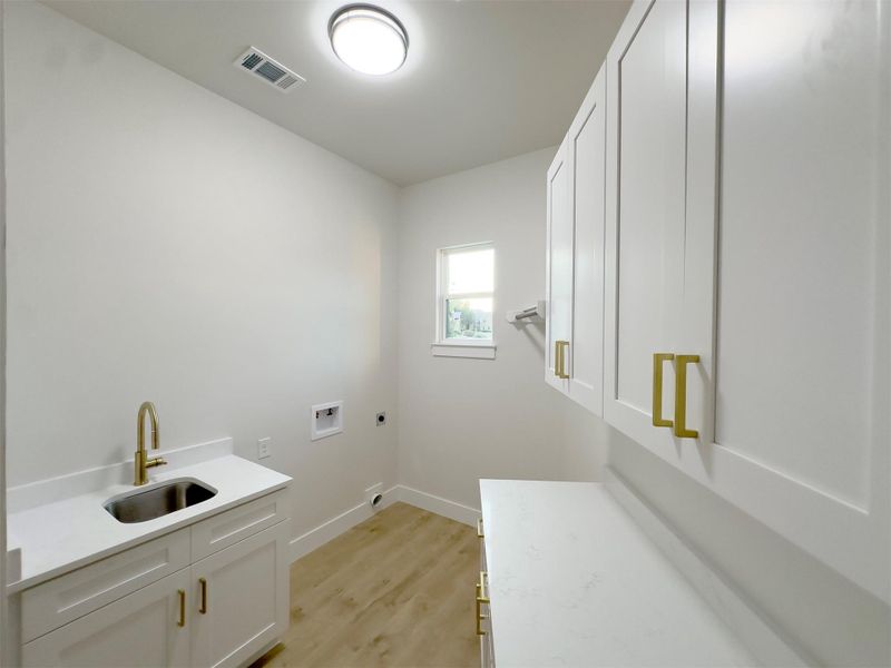 A functional laundry space highlights clean cabinetry and a built-in sink on wood-style flooring. A functional laundry space highlights clean cabinetry and a built-in sink on wood-style flooring.