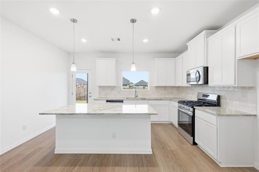 Kitchen with appliances with stainless steel finishes, decorative backsplash, white cabinets, light wood-type flooring, and a kitchen island