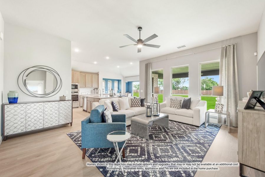 Open-concept living room with ceiling fan, light wood floors, and kitchen visible in background Open-concept living room with ceiling fan, light wood floors, and kitchen visible in background