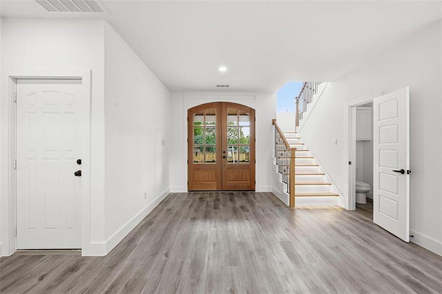 Foyer entrance with french doors, stairs, light wood-style flooring, arched walkways, and recessed lighting