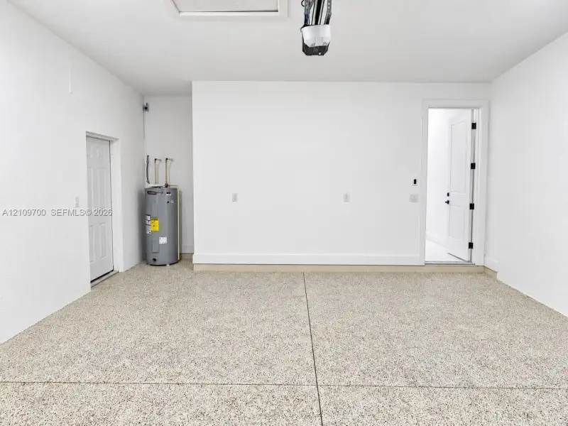 Garage interior featuring finished epoxy flooring, white painted walls, two access doors, and an integrated water heater
