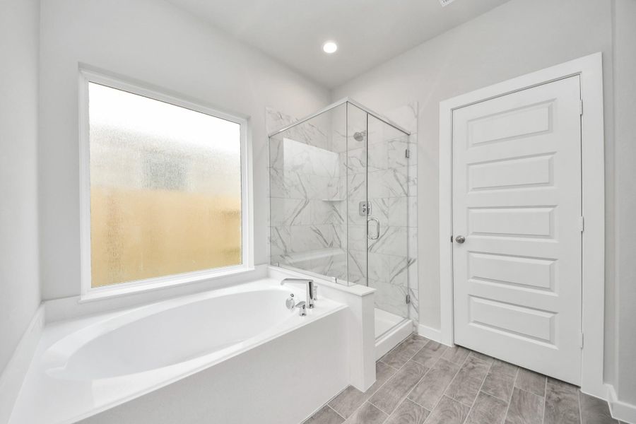 Indulge in a spa-like retreat within the confines of this primary bathroom. Delight in a spacious walk-in shower enveloped in stylish tile surround, unwind in a separate garden tub adorned with custom detailing. Sample photo of completed home with similar floor plan. Actual colors and selections may vary.