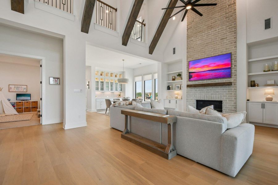 This expansive living area features vaulted ceilings with exposed beams, light hardwood flooring, and an impressive brick fireplace with a mantel This expansive living area features vaulted ceilings with exposed beams, light hardwood flooring, and an impressive brick fireplace with a mantel