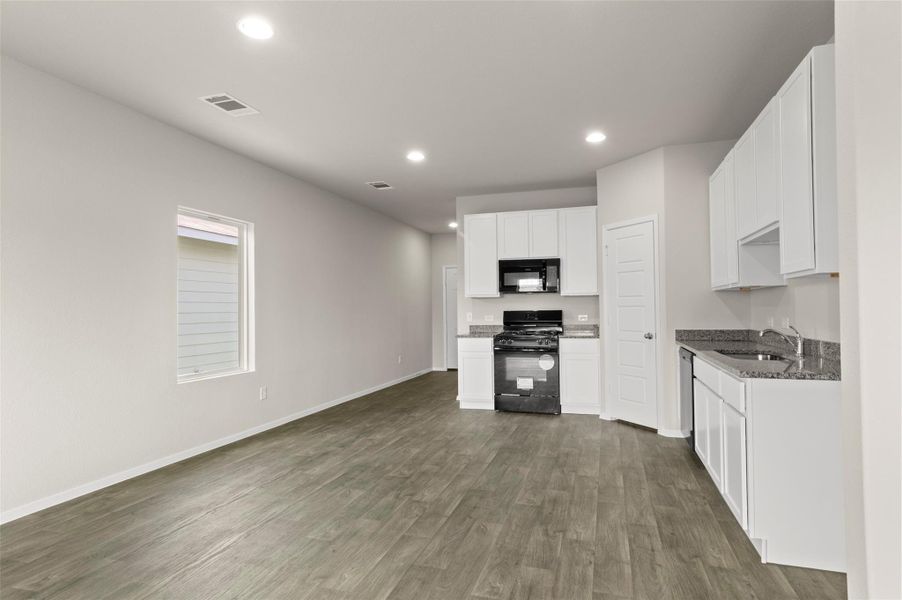 Kitchen with black appliances, recessed lighting, dark wood-style floors, white cabinetry, and dark stone countertops