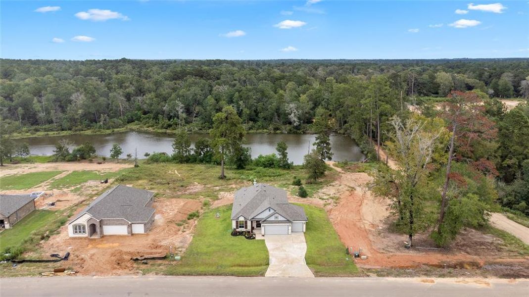 An aerial view of this beautiful new home with new construction homes near the scenic neighborhood lake, surrounded by lush greenery, offering a blend of modern living and natural beauty.