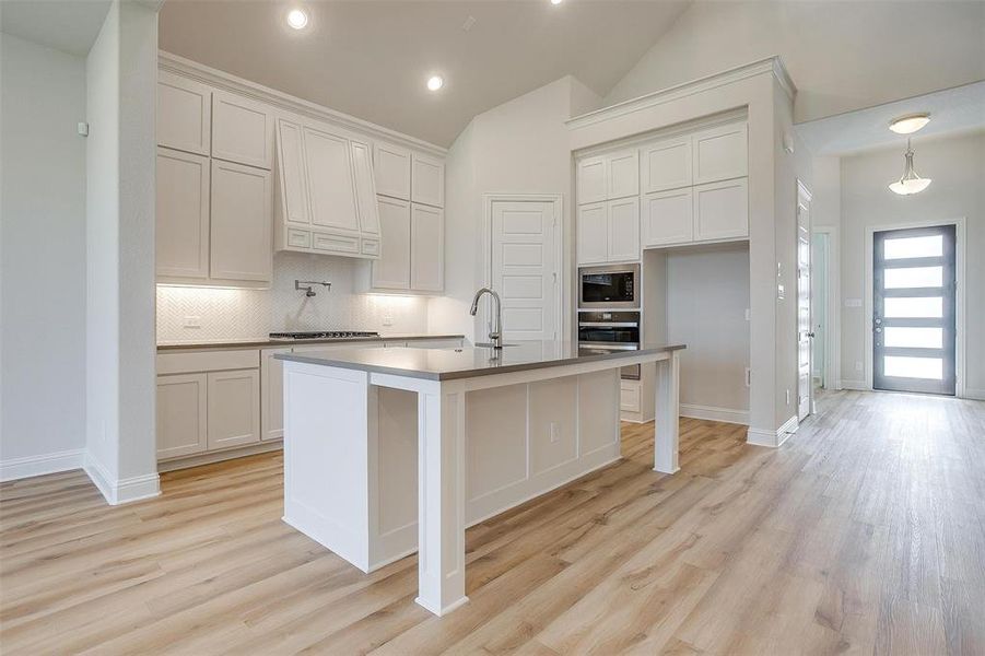 Kitchen with white cabinetry, decorative light fixtures, tasteful backsplash, light wood-type flooring, and appliances with stainless steel finishes