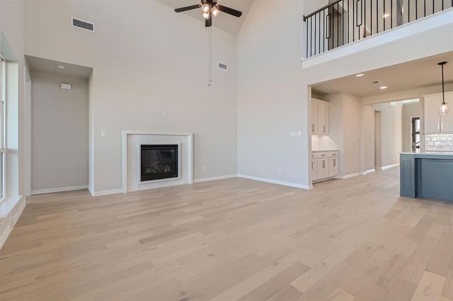 Unfurnished living room featuring light wood-type flooring, high vaulted ceiling, and ceiling fan