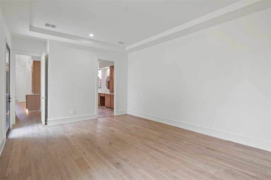 Unfurnished bedroom with light wood-type flooring, a tray ceiling, ensuite bath, and recessed lighting Unfurnished bedroom with light wood-type flooring, a tray ceiling, ensuite bath, and recessed lighting