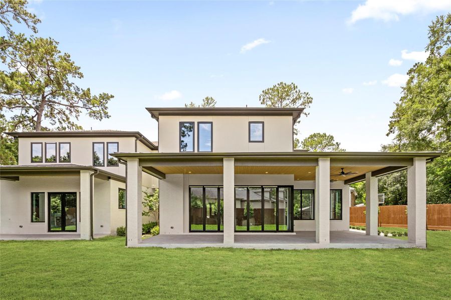 The rear exterior features a spacious covered outdoor living area, expansive lawn, and seamless indoor-outdoor connection.