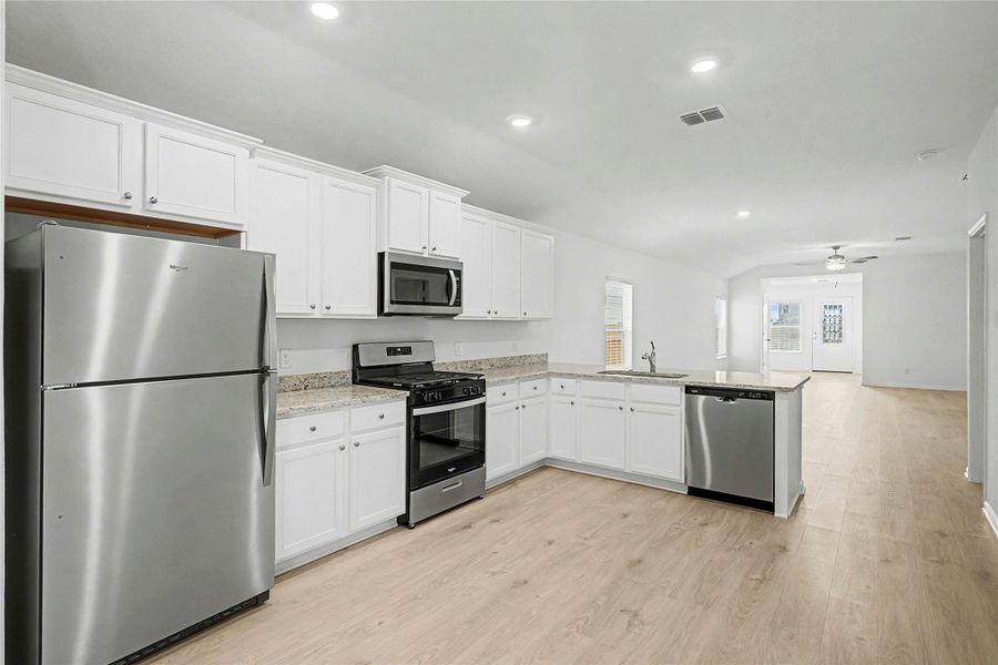 A streamlined kitchen presents stainless steel appliances and abundant white cabinetry, seamlessly flowing into the adjacent living space.