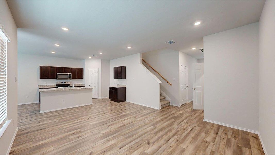 Open-concept living area featuring wood-finish flooring, recessed lighting, and a modern kitchen with dark cabinetry Open-concept living area featuring wood-finish flooring, recessed lighting, and a modern kitchen with dark cabinetry