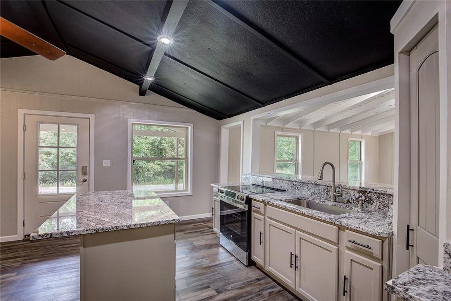 Kitchen with sink, stainless steel range with electric cooktop, vaulted ceiling with beams, light stone counters, and a center island