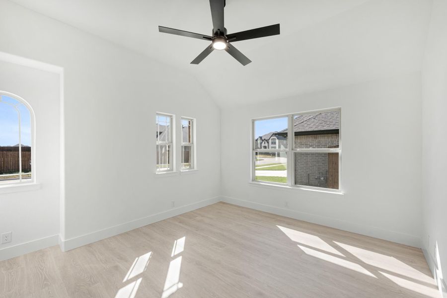 Empty bedroom with vaulted ceiling, black ceiling fan, light wood floors, and multiple windows