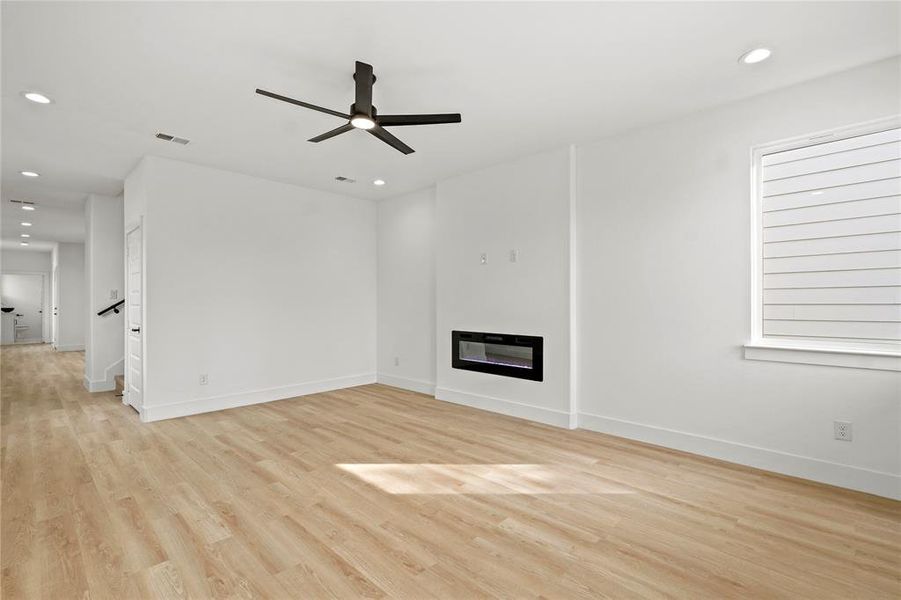 Unfurnished living room with light wood-style floors, recessed lighting, a glass covered fireplace, ceiling fan, and baseboards Unfurnished living room with light wood-style floors, recessed lighting, a glass covered fireplace, ceiling fan, and baseboards