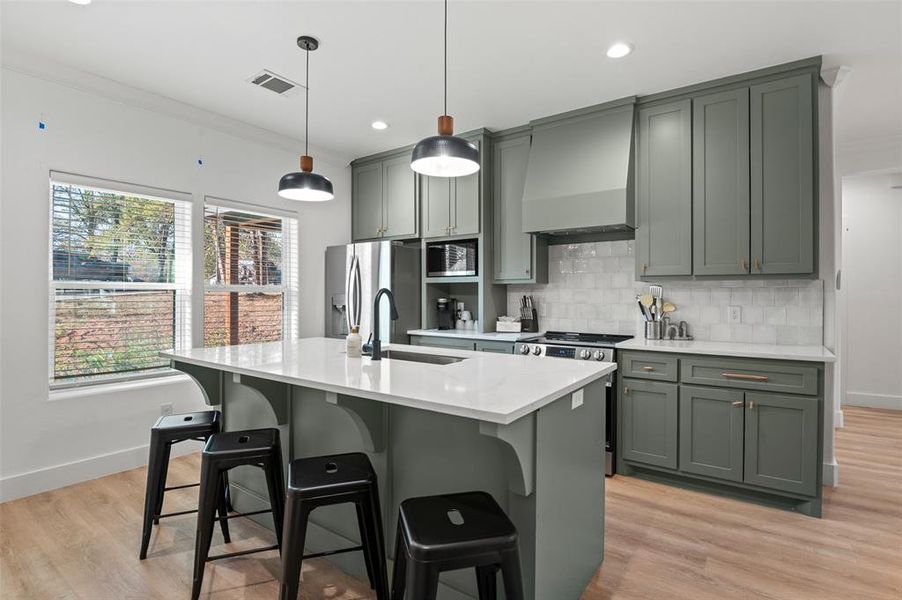 Kitchen with custom range hood, stainless steel appliances, a kitchen island with sink, crown molding, and sink