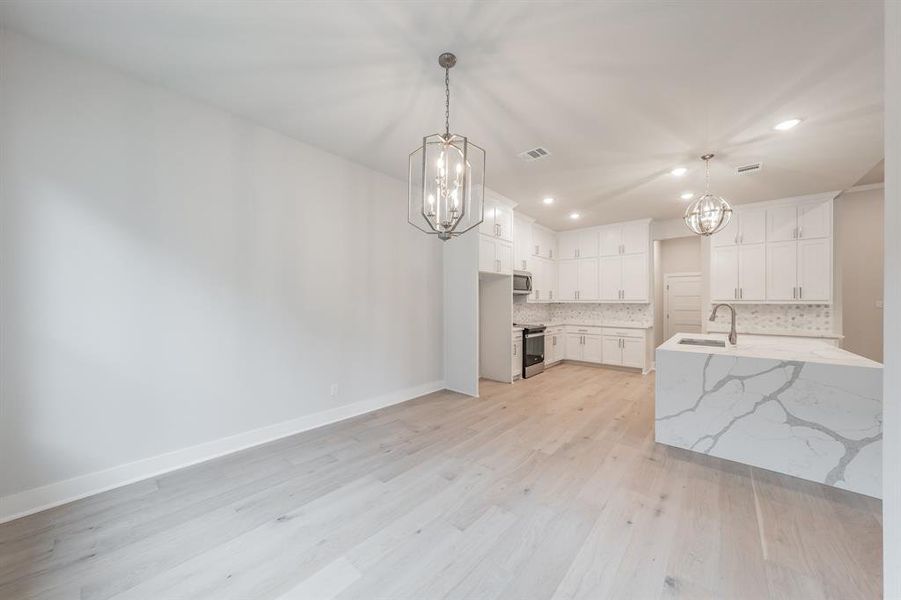 Kitchen featuring a chandelier, tasteful backsplash, light stone countertops, recessed lighting, and white cabinets