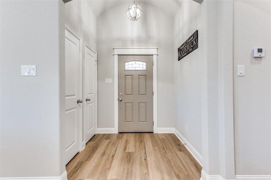 Entryway featuring light wood-type flooring, vaulted ceiling, and a chandelier Entryway featuring light wood-type flooring, vaulted ceiling, and a chandelier