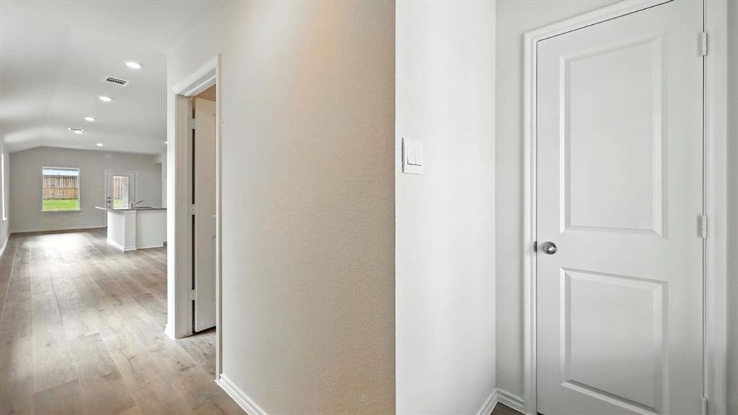 Interior hallway with light wood-finish flooring, white trim, and recessed lighting leading to an open-concept living area Interior hallway with light wood-finish flooring, white trim, and recessed lighting leading to an open-concept living area