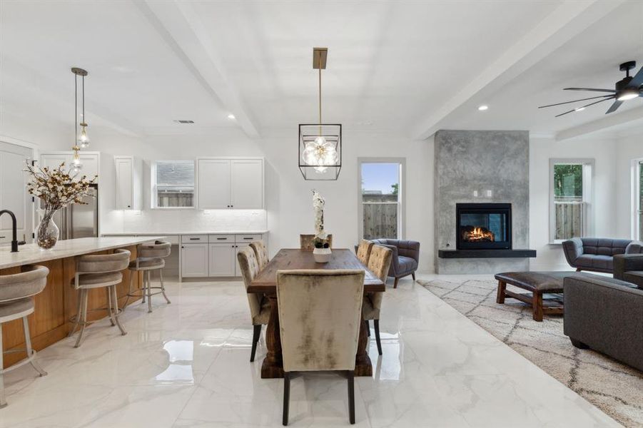 Dining space with a healthy amount of sunlight, ceiling fan with notable chandelier, a fireplace, and beamed ceiling