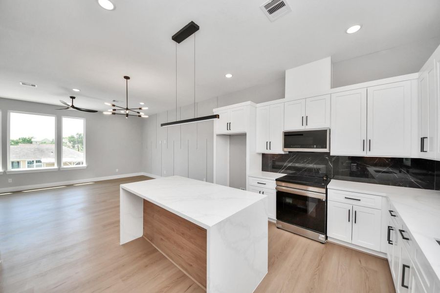 Modern designer kitchen with sleek quartz countertops, custom cabinetry, black marble backsplash, & a striking waterfall island overlooking the open-concept living space.