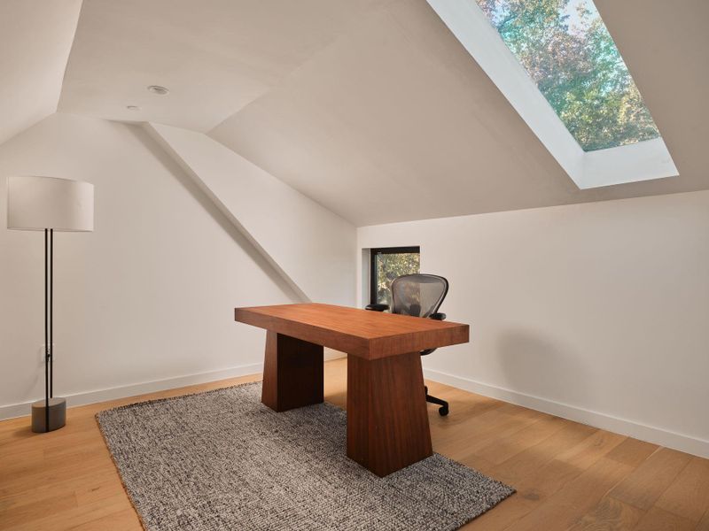 Unfurnished office with light wood-style floors, lofted ceiling, and a skylight