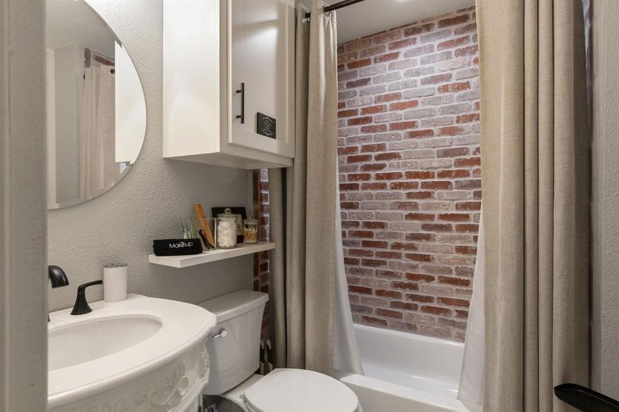 Full bathroom with shower / bath combo, a textured wall, brick wall, and vanity Full bathroom with shower / bath combo, a textured wall, brick wall, and vanity