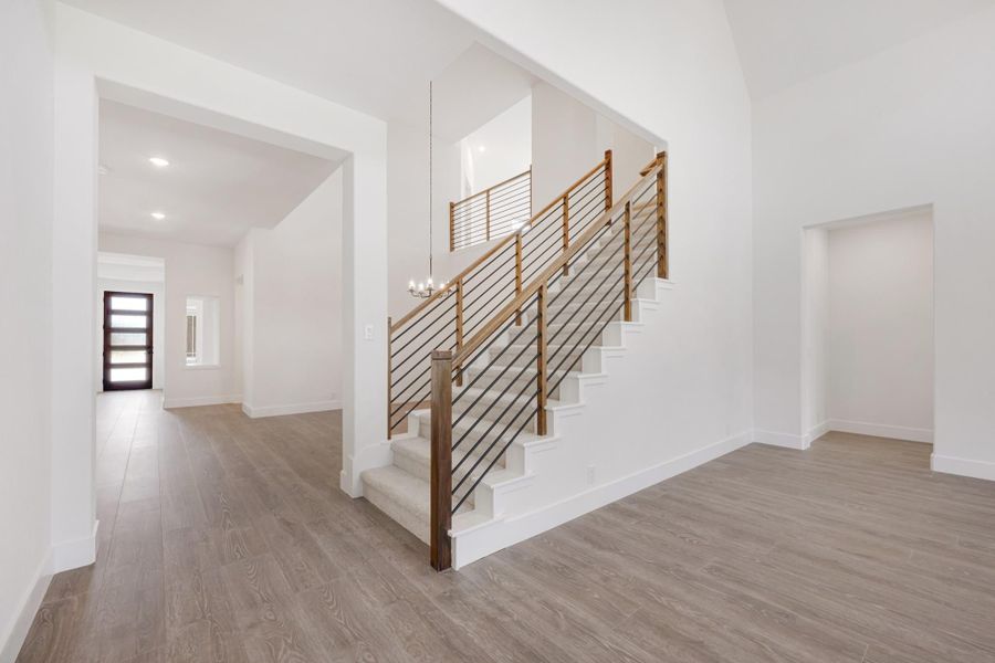 Open foyer with staircase featuring wood and metal railing, chandelier, and light hardwood floors