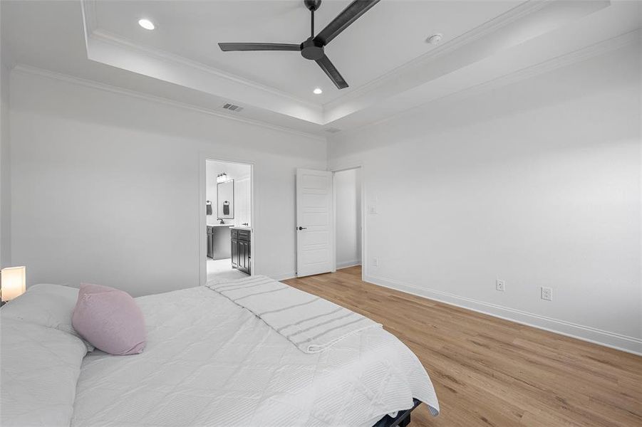 Bedroom featuring a tray ceiling, light wood finished floors, ceiling fan, ornamental molding, and connected bathroom Bedroom featuring a tray ceiling, light wood finished floors, ceiling fan, ornamental molding, and connected bathroom