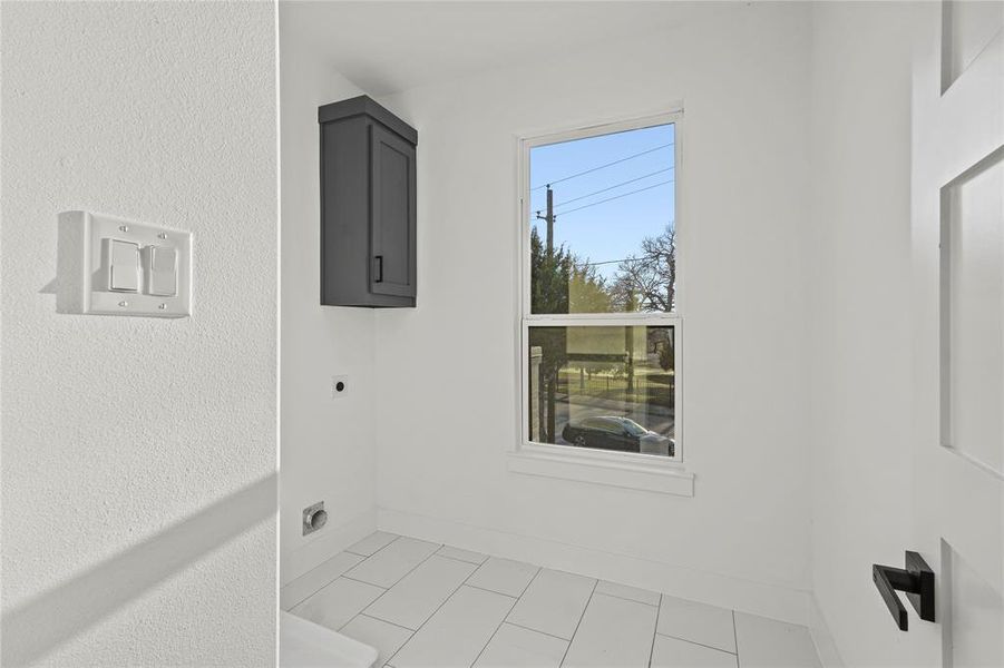 Clothes washing area with baseboards, light tile patterned flooring, cabinet space, and hookup for an electric dryer