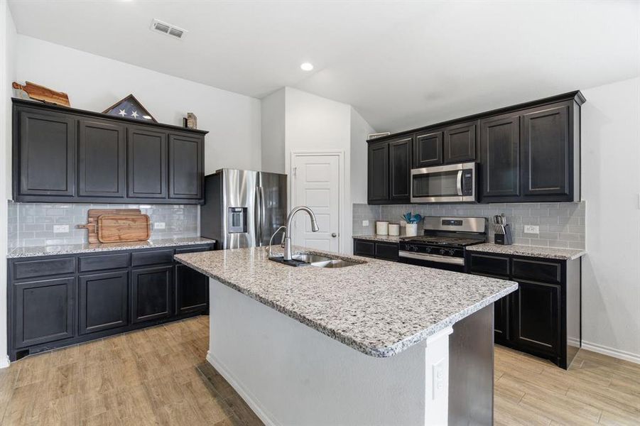 Kitchen with tasteful backsplash, stainless steel appliances, light stone counters, light wood-style floors, and lofted ceiling